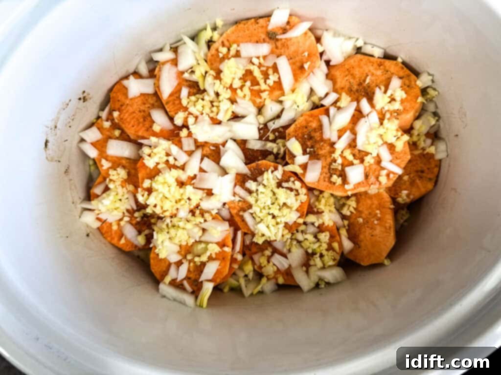 Chopped onion, garlic, and ginger evenly scattered over the sweet potatoes in the slow cooker.