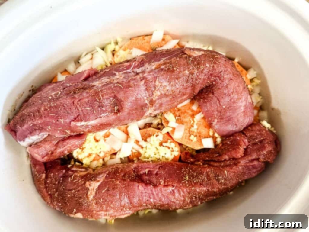Pork tenderloins, seasoned and placed on top of the vegetables in the slow cooker.