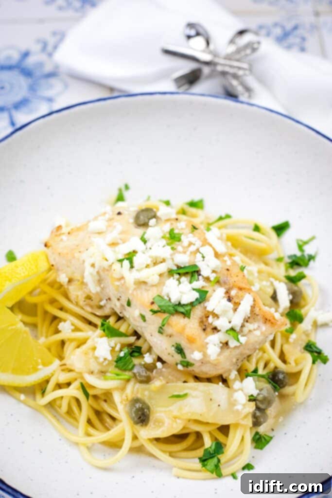 A vibrant pasta dish generously topped with Skillet Chicken with Artichokes, Lemon, and Feta, beautifully presented on a round white plate, garnished with fresh herbs.