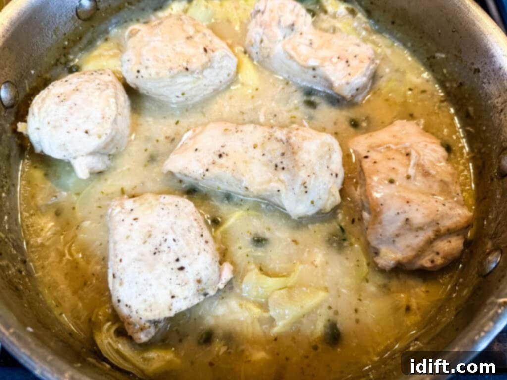 Chicken pieces cooking in a pan with a light, simmering sauce, garnished with capers and sliced onions.