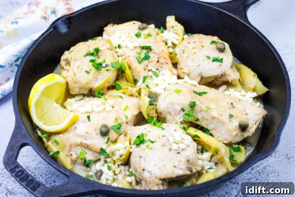 A close-up of tender chicken pieces nestled among artichokes, vibrant capers, and fresh herbs in a sleek black pan, elegantly garnished with bright lemon wedges and a sprinkle of chopped parsley, ready to be served.