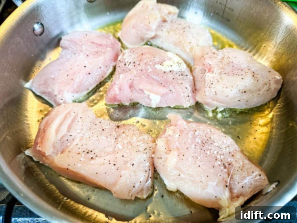Raw chicken pieces, seasoned with a generous sprinkle of salt and pepper, being seared in a hot metal pan with olive oil to achieve a golden-brown crust.