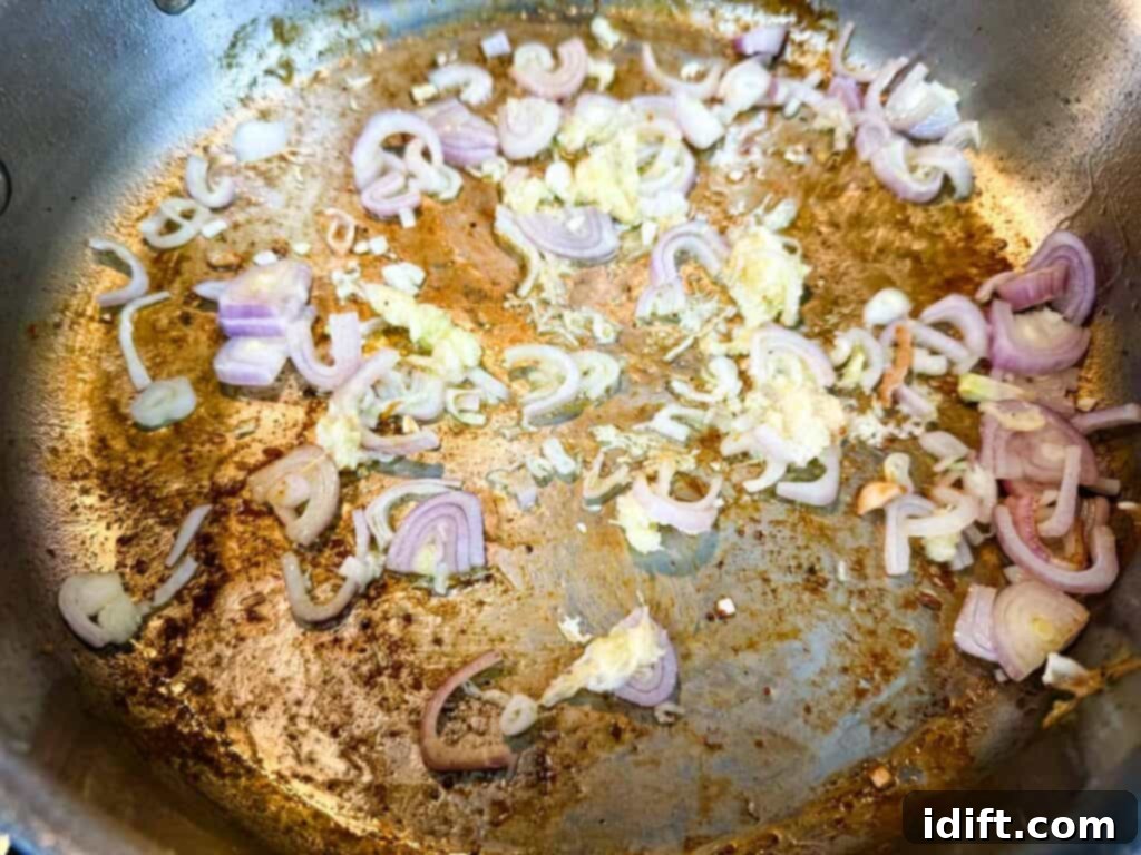 Thinly sliced shallots and minced garlic gently sautéing in a hot skillet, releasing their fragrant aromas.