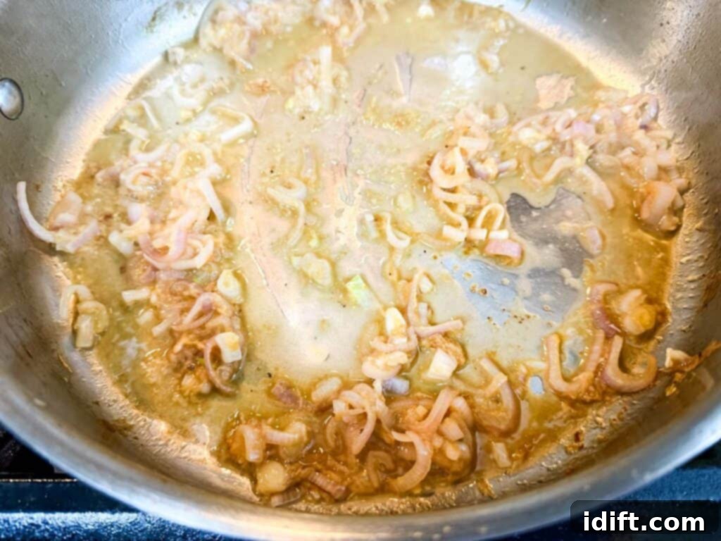 Sliced shallots and minced garlic simmering in a stainless steel pan as white wine is added to deglaze, lifting browned bits from the bottom.