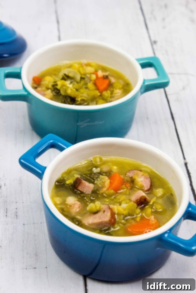 A close-up of two blue ceramic bowls filled with rich, green split pea soup, generously studded with chunks of ham and smoked sausage, ready to be enjoyed.