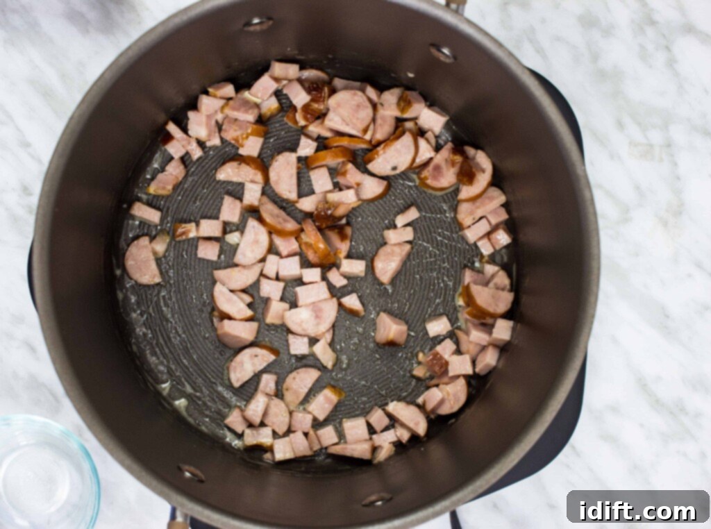 Smoked sausage browning in melted butter within a skillet, developing a golden crust and releasing its rich aroma, preparing for a hearty soup.