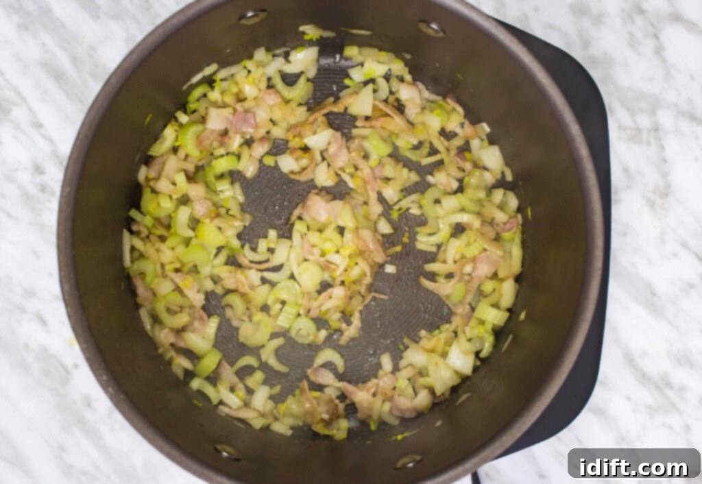 Diced onions, carrots, and celery are sautéing in a pot with bacon, becoming soft and translucent, forming the aromatic base for the Split Pea, Ham & Sausage Soup.