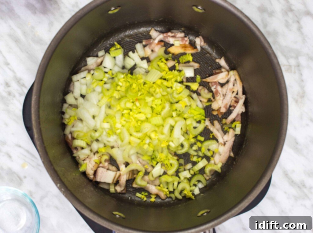 Freshly diced onions, celery, and crispy bacon are being combined in a large pot, sizzling gently as they begin to cook down and release their flavors.