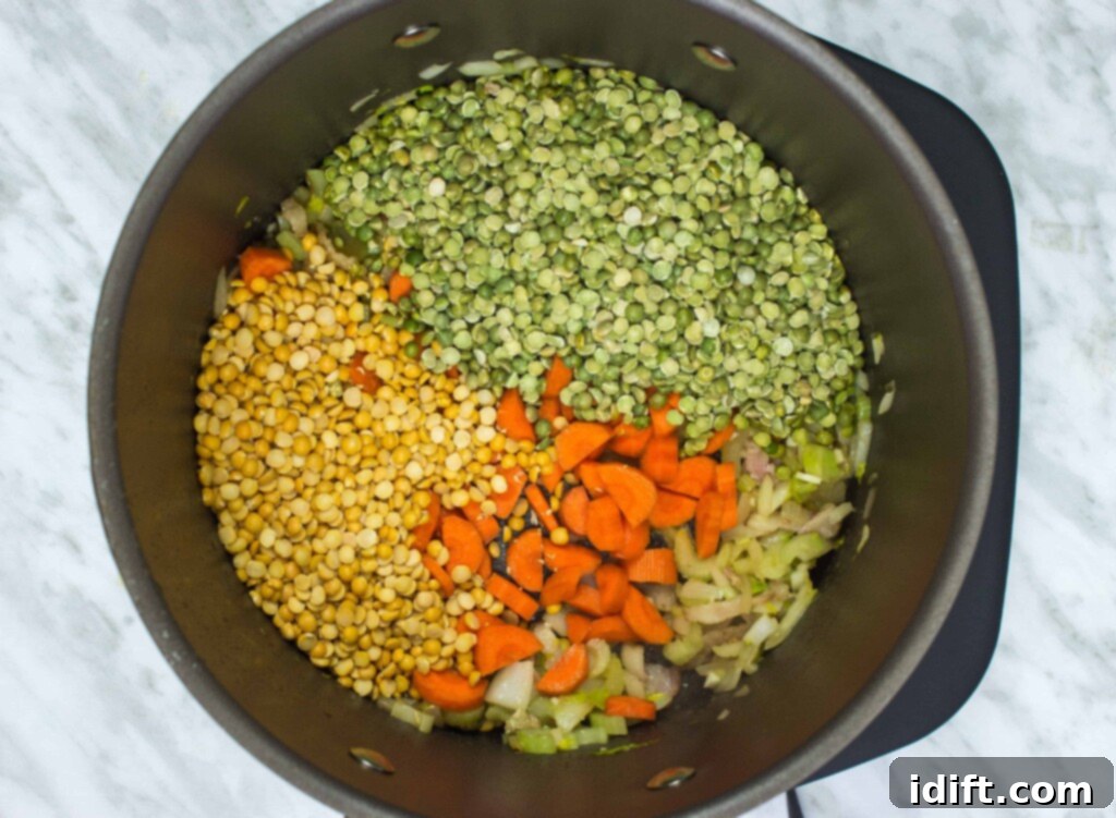 Dried green and yellow split peas, fresh kale, and chopped carrots are being added to a large pot, ready to be combined with savory broth for a wholesome soup.