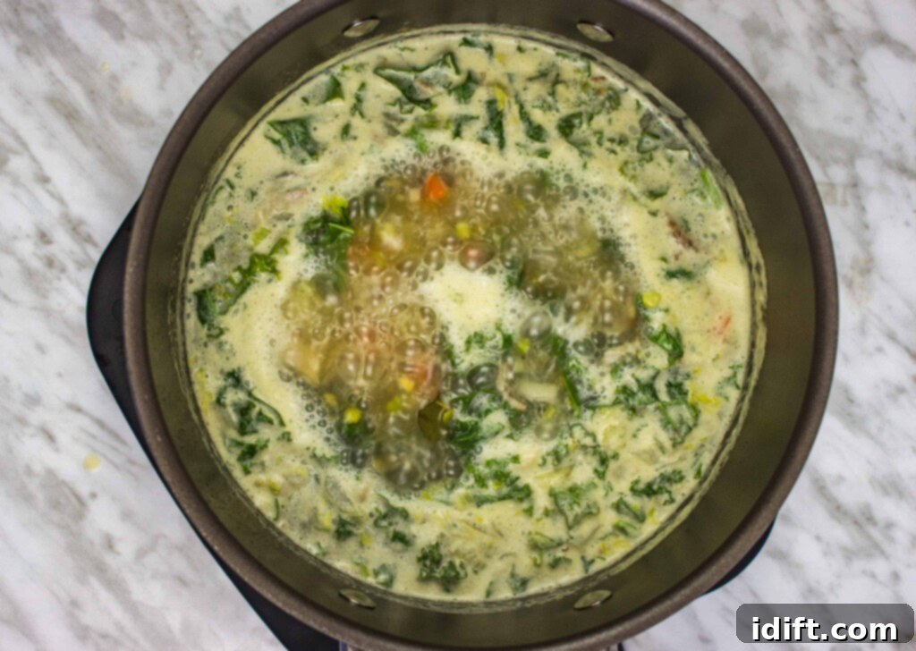 A large pot of Split Pea, Ham & Sausage Soup gently simmers on the stovetop, the peas and vegetables softening and flavors melding together.