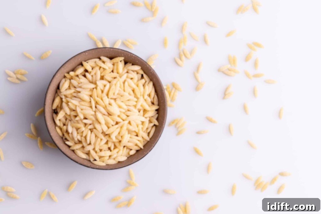 Velvety Spinach and Tomato Orzo 4 Uncooked orzo pasta in a ceramic bowl with some grains scattered on a rustic wooden surface, highlighting its rice-like shape.