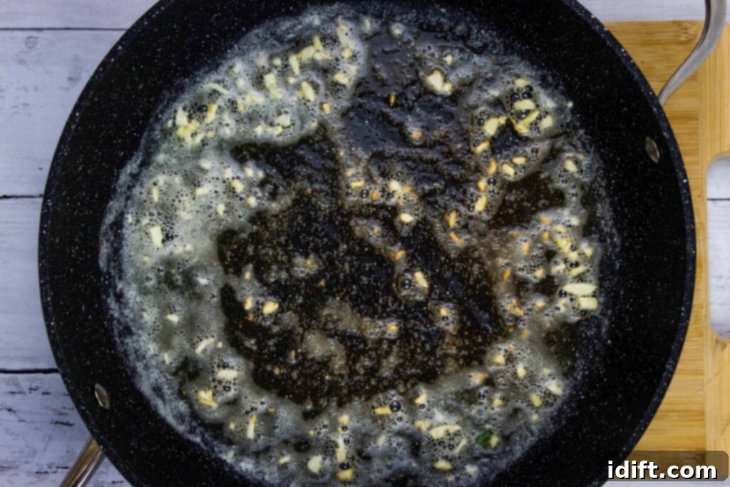 Velvety Spinach and Tomato Orzo 7 Garlic actively sautéing in melted butter within a skillet, releasing its fragrant aroma.