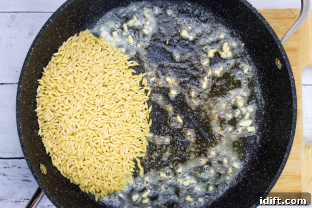 Velvety Spinach and Tomato Orzo 8 Uncooked orzo being toasted in a skillet alongside garlic butter, turning slightly golden.