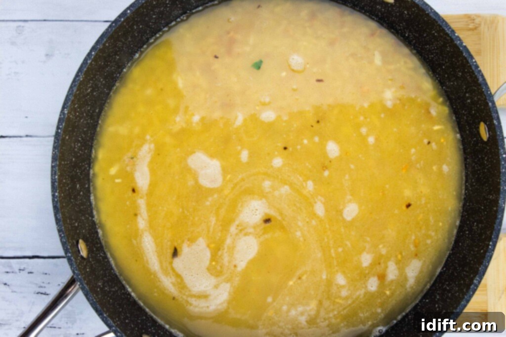 Velvety Spinach and Tomato Orzo 10 Chicken broth being poured into the skillet with toasted orzo, ready to be covered and simmered.