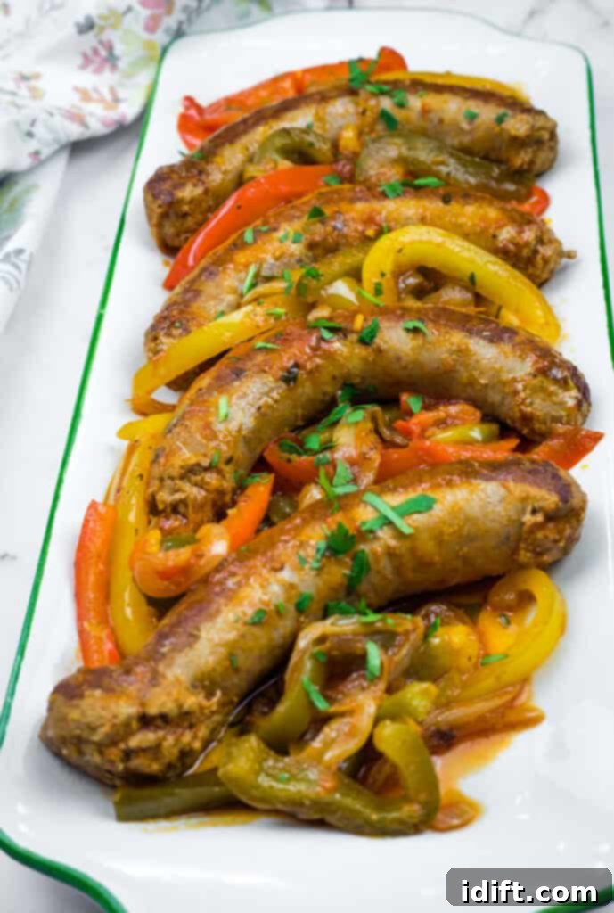 Slow Cooker Sausage & Peppers on a rectangular plate with sliced red, yellow, and green bell peppers, garnished with chopped herbs. A perfect, vibrant meal.