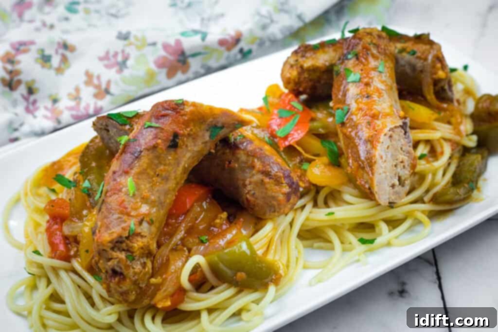 Sausages on spaghetti with bell peppers, garnished with herbs, served on a rectangular white plate, highlighting a classic pairing.