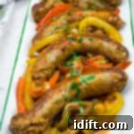 Slow Cooker Sausage & Peppers on a rectangular plate with sliced red, yellow, and green bell peppers, garnished with chopped herbs.