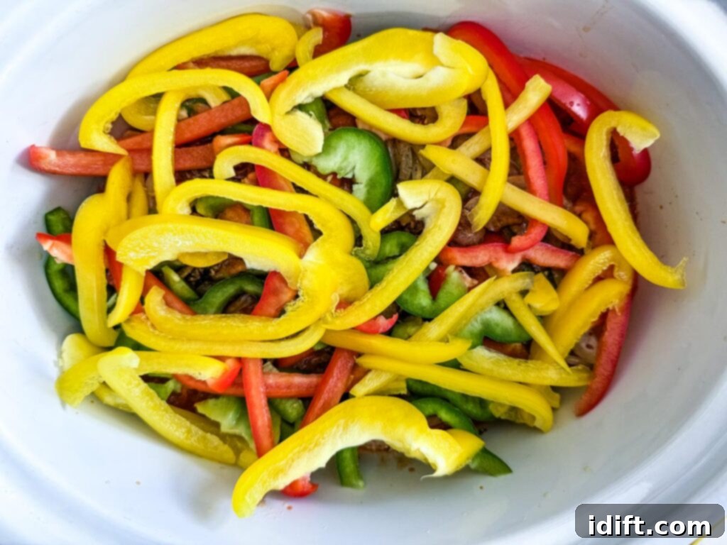 Sliced red, yellow, and green bell peppers in a white bowl, ready to be added to the slow cooker.