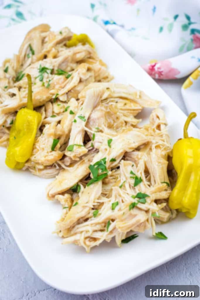 Slow Cooker Mississippi Chicken with fresh herbs and yellow peppers on a white rectangular plate, presented on a light surface with a floral cloth in the background.