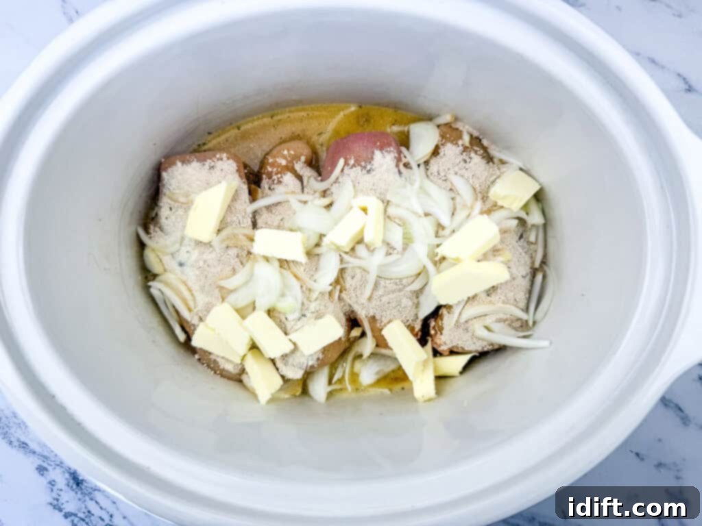 Raw chicken breasts topped with sliced onions, butter, and seasoning in a slow cooker.