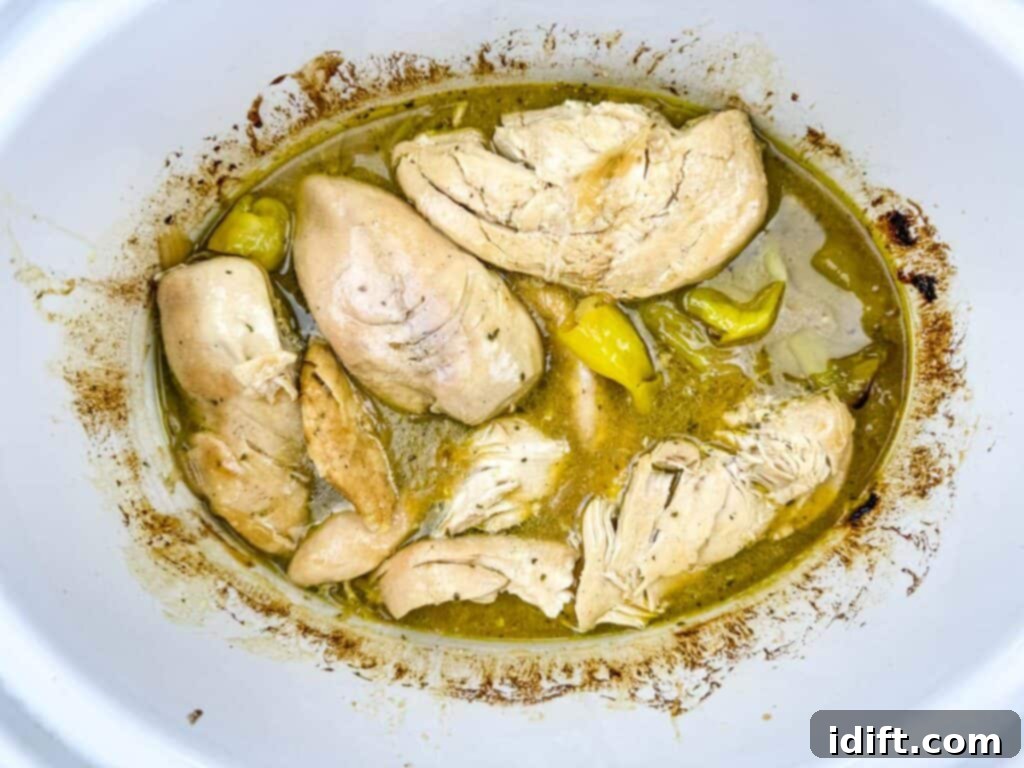 Chicken breasts cooked in broth with pepperoncini peppers in a slow cooker.