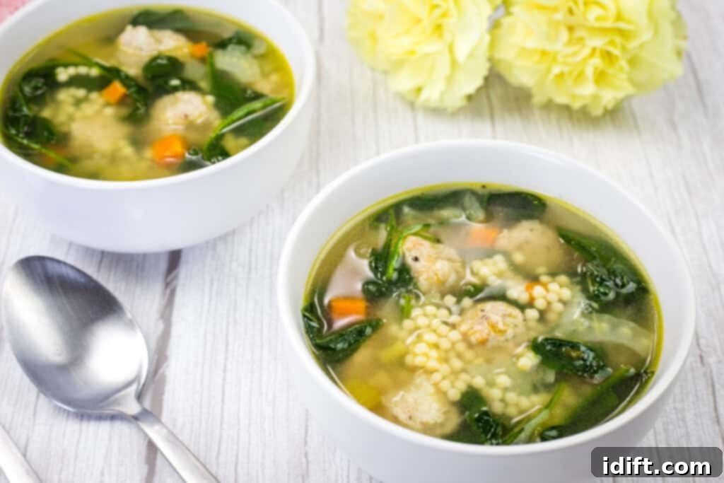 Two bowls of Italian Wedding Soup with spoon and flower on a white wooden table.
