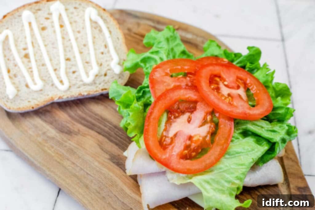 Open-faced sandwich with turkey, lettuce, and sliced tomatoes on one slice of bread, with mayo on the other on a wooden board.