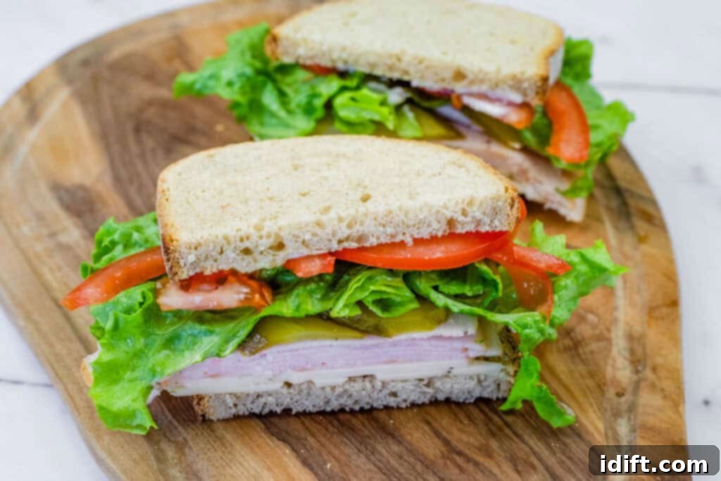 Turkey sandwich with lettuce, tomatoes, pickles, and cheese on whole-grain bread, cut in half and served on a wooden board.