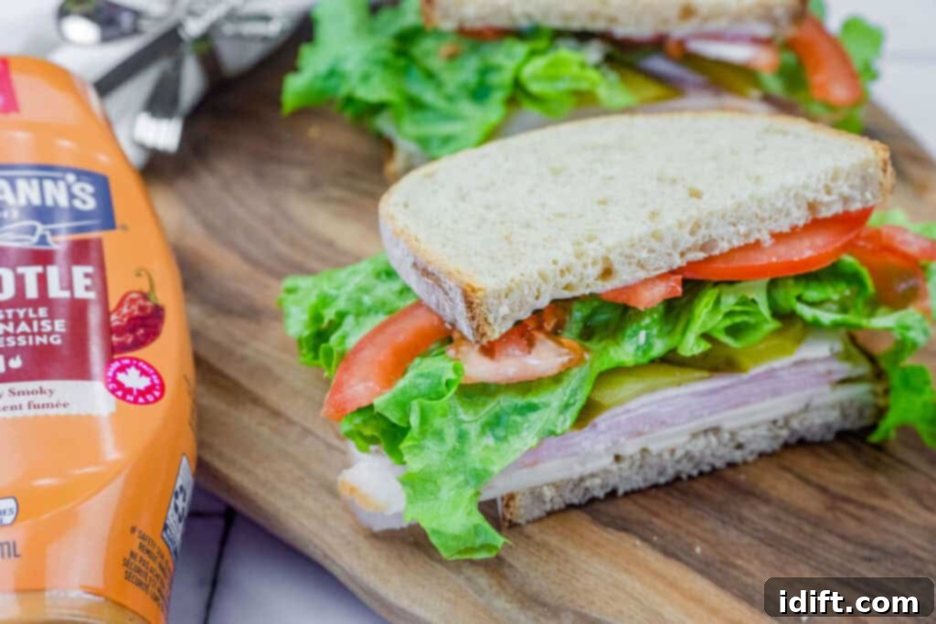 Turkey sandwich with lettuce, tomato, pickles, and cheese on whole-grain bread, with Hellmann's Chipotle mayo beside it.