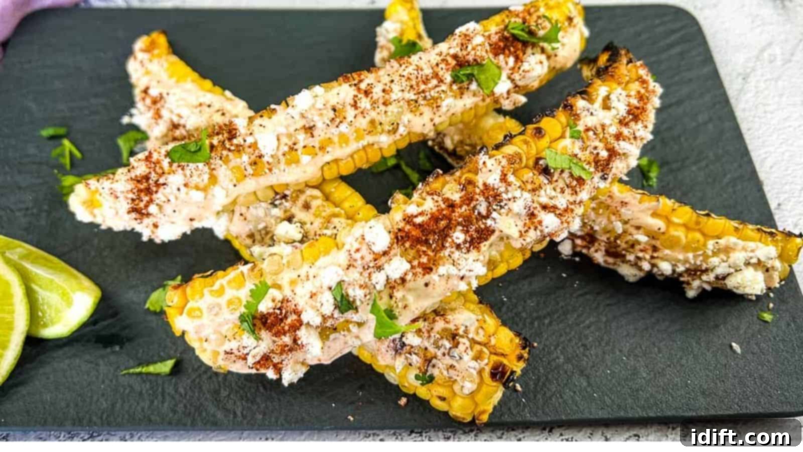 17 Effortless Sides That Prove Dinner Doesn't Have To Be Hard 8 Grilled corn on the cob pieces topped with cheese, chili powder, and cilantro, served on a black slate plate with lime wedges on the side.