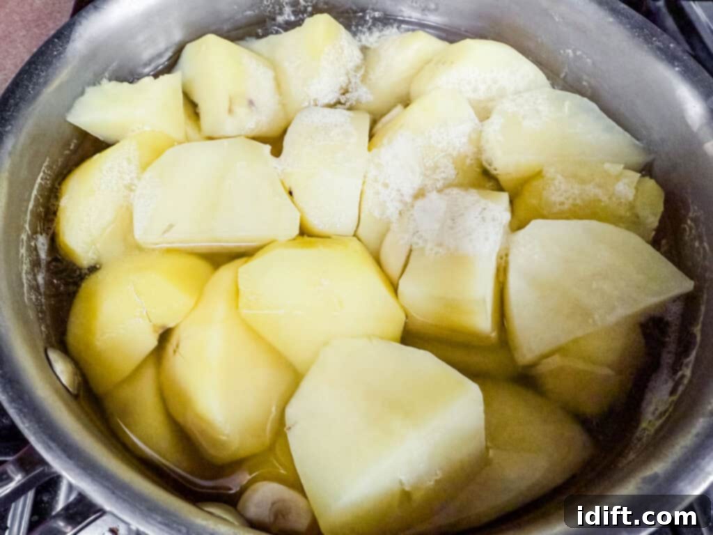 Pot of peeled and chopped potatoes boiling in water, with foam forming on the surface.