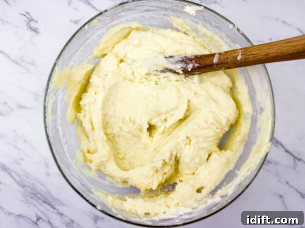A glass bowl filled with creamy, smooth mashed potatoes being mixed with a wooden spoon.