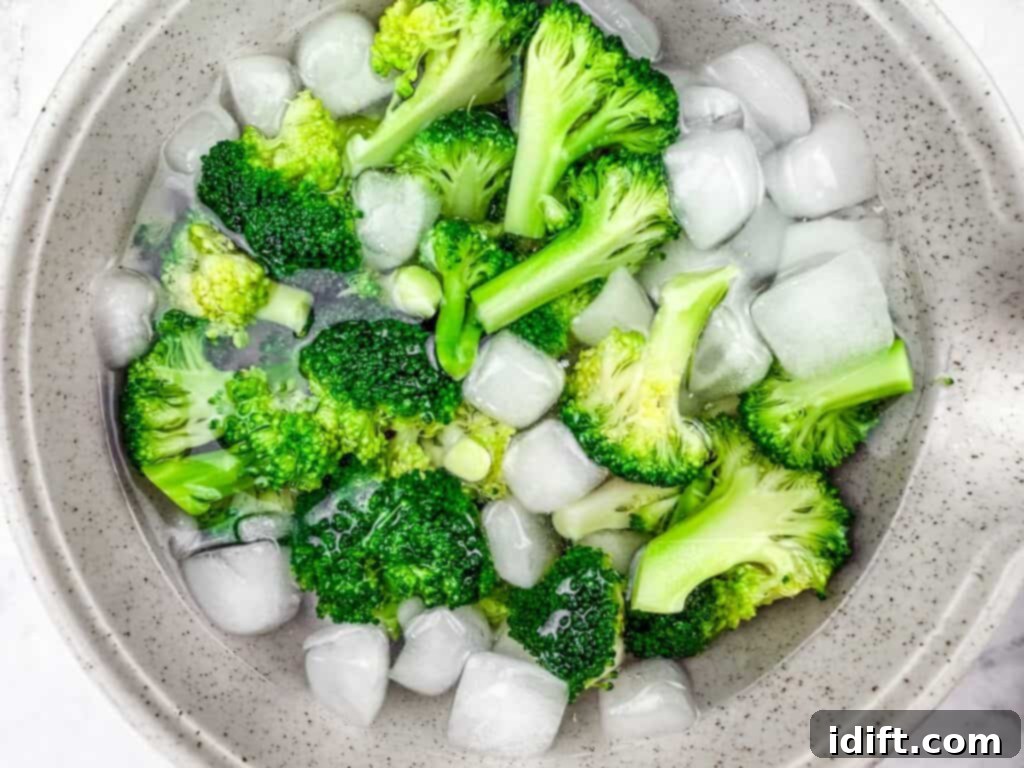Freshly blanched broccoli florets in an ice water bath to preserve their vibrant green color and crisp texture, ready to be added to the skillet.