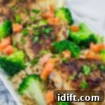 A Lemon Chicken Orzo Skillet with Broccoli dish featuring golden-brown seasoned chicken thighs on a bed of orzo pasta, garnished with fresh broccoli florets, diced tomatoes, chopped parsley, and lemon slices in the background.
