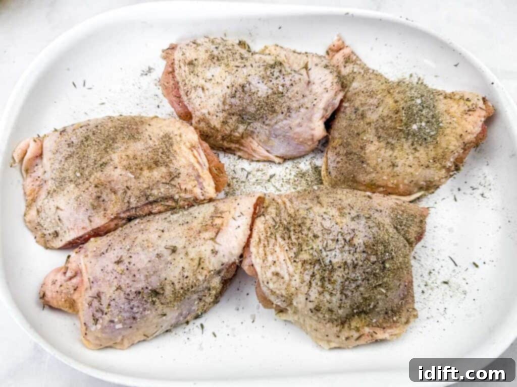 Raw chicken thighs seasoned generously with a blend of herbs and spices, arranged on a white plate, showcasing perfect readiness for searing.