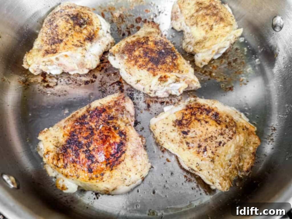 Chicken thighs being expertly seared in a stainless steel pan, developing a beautiful golden-brown, crispy skin with flavorful seasonings, ready for the next step.