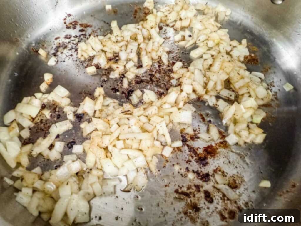 Chopped onions sautéing in a stainless steel pan, absorbing the flavorful browned bits left from searing the chicken, creating a rich base.
