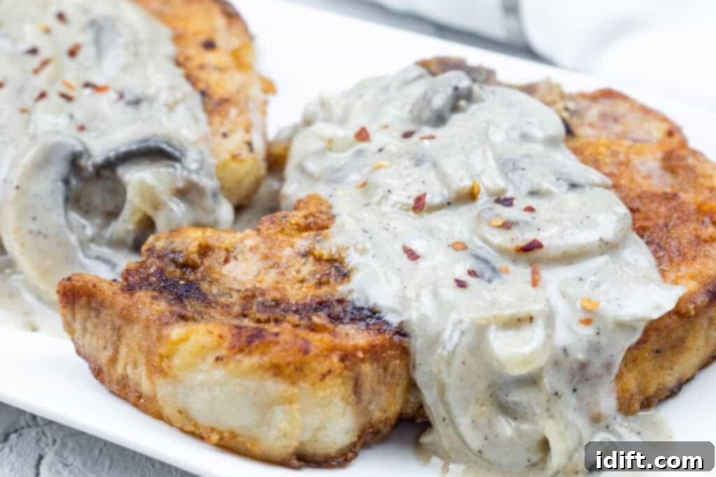 Two Smothered Pork Chops with Onions & Mushrooms, garnished with crushed red pepper, served on a white plate.