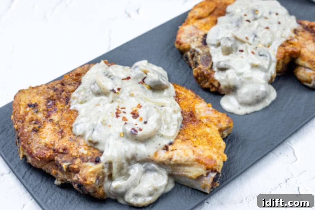 Two Smothered Pork Chops with Onions & Mushrooms on a black rectangular plate.