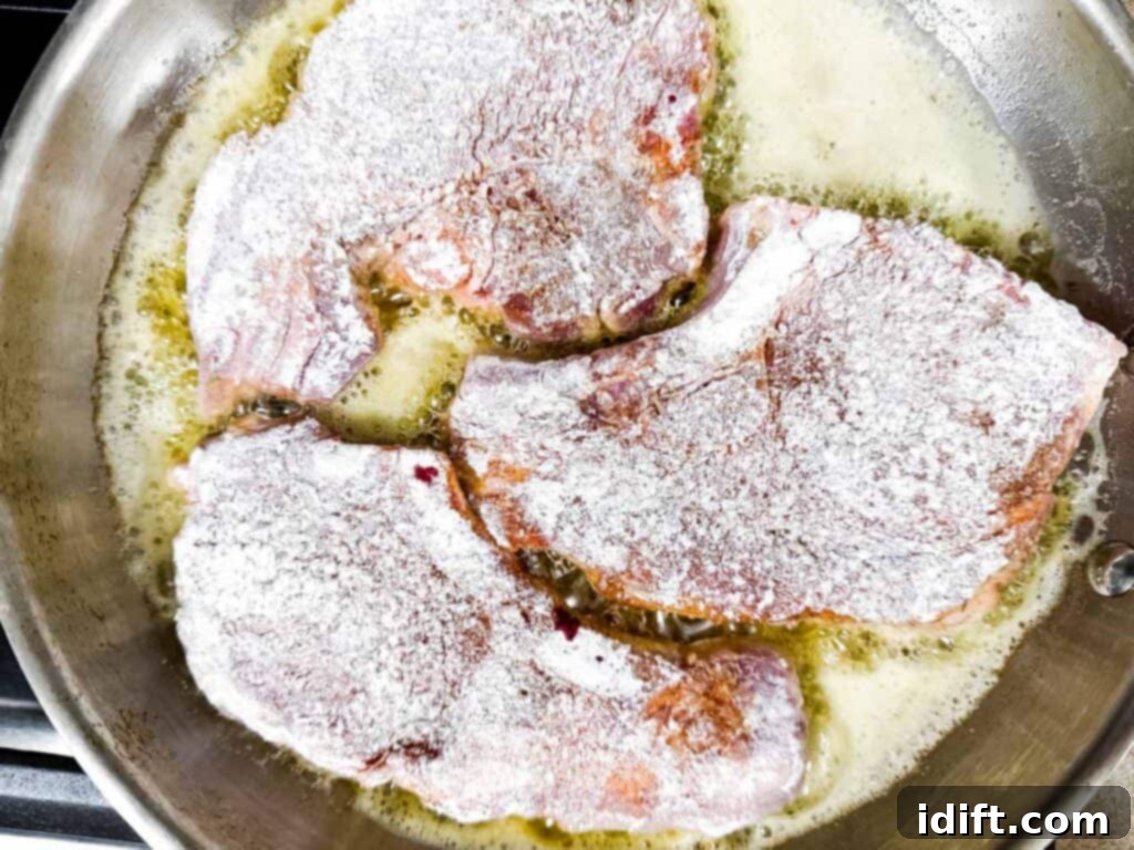 Three flour-coated meat chops cooking in a pan with bubbling oil.