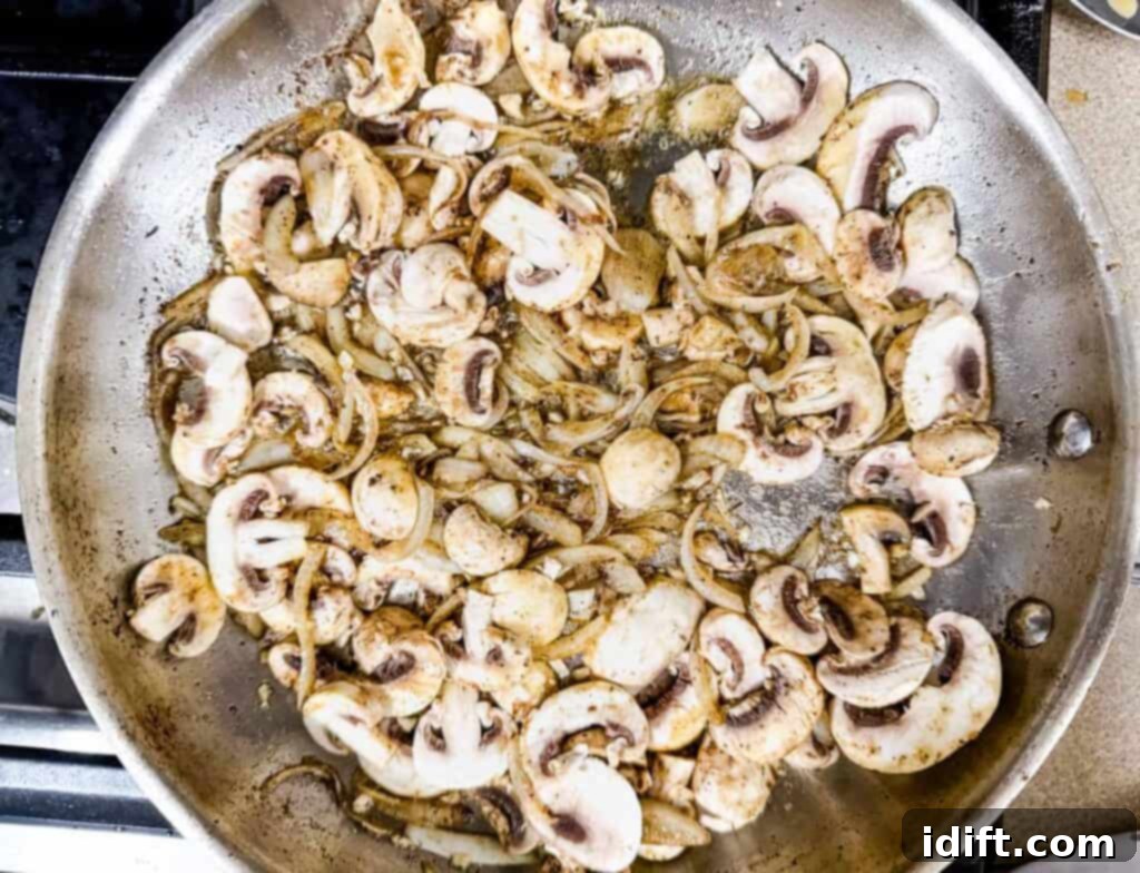 Sliced mushrooms and onions sautéing in a large skillet.