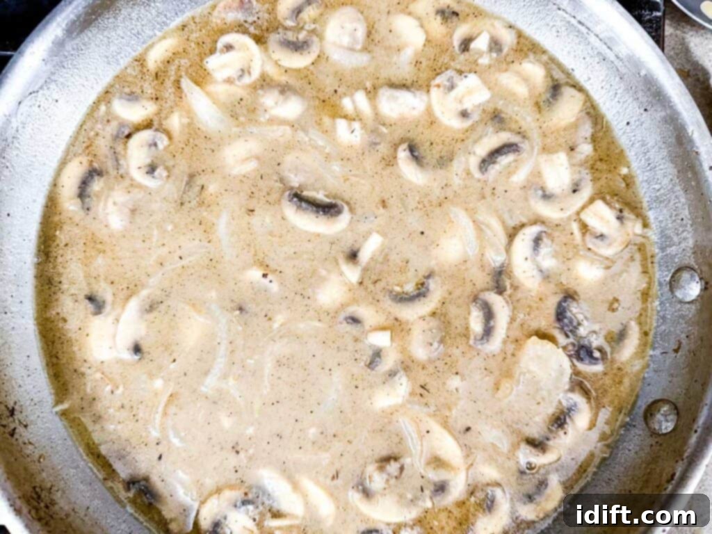 A skillet filled with creamy mushroom sauce, featuring sliced mushrooms and onions in a thick, beige liquid.