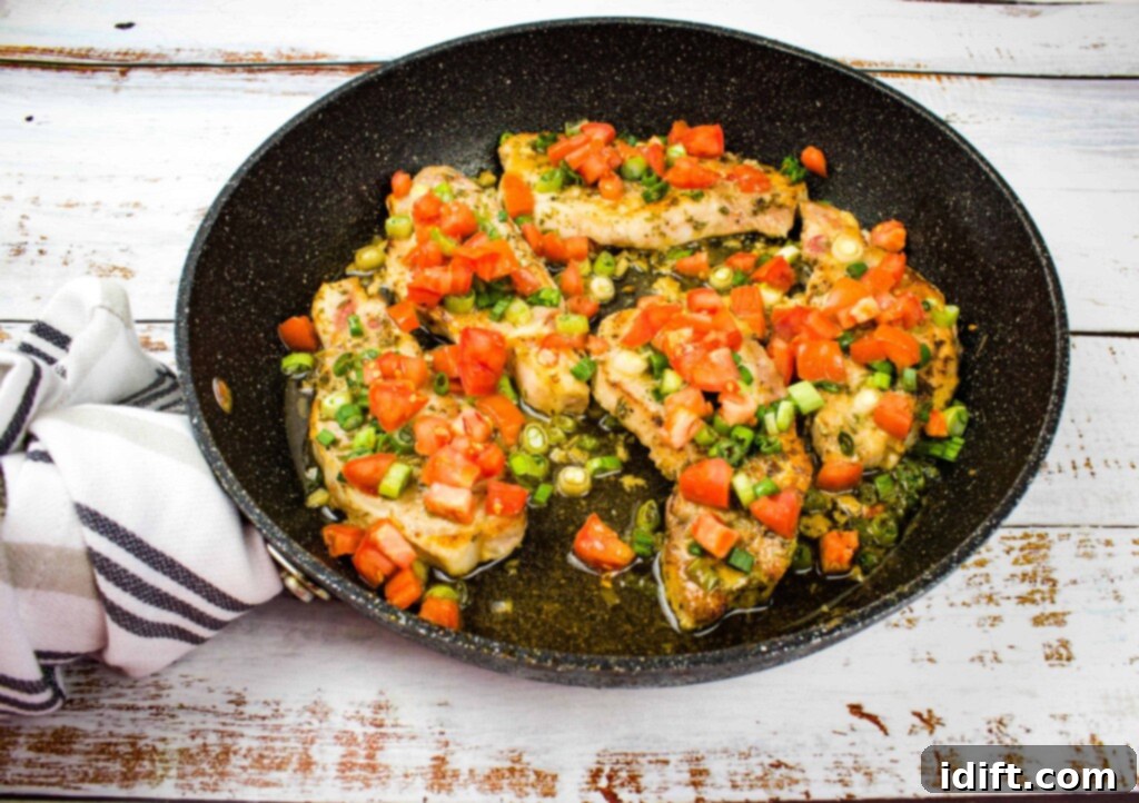 Pork Chops with Tomato & Green onion relish beautifully plated in a black skillet, ready to serve.