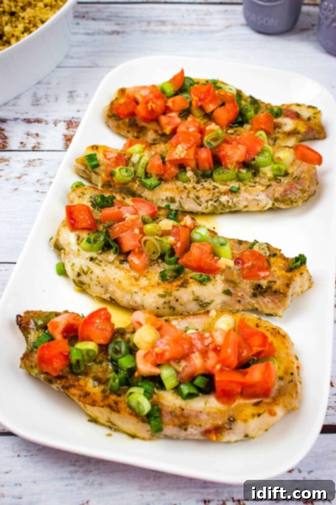 A close up of Pork chops with Tomato & Green Onion Relish served on a white platter with couscous visible in the blurred background.