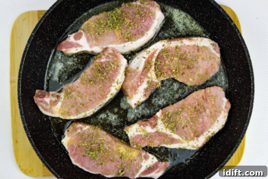 Seasoned pork chops are placed in a hot skillet, ready to be seared on the first side.
