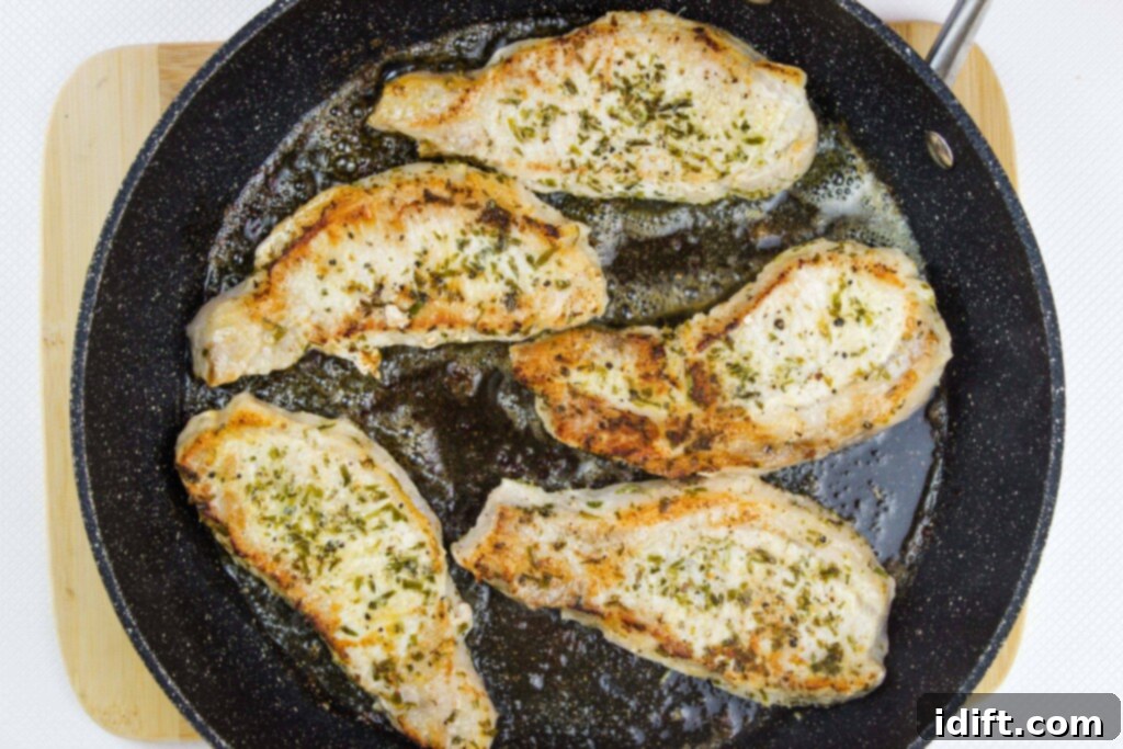 Pork chops, seared on one side to a golden brown, are flipped in a black skillet, creating a delicious foundation for the pan sauce.
