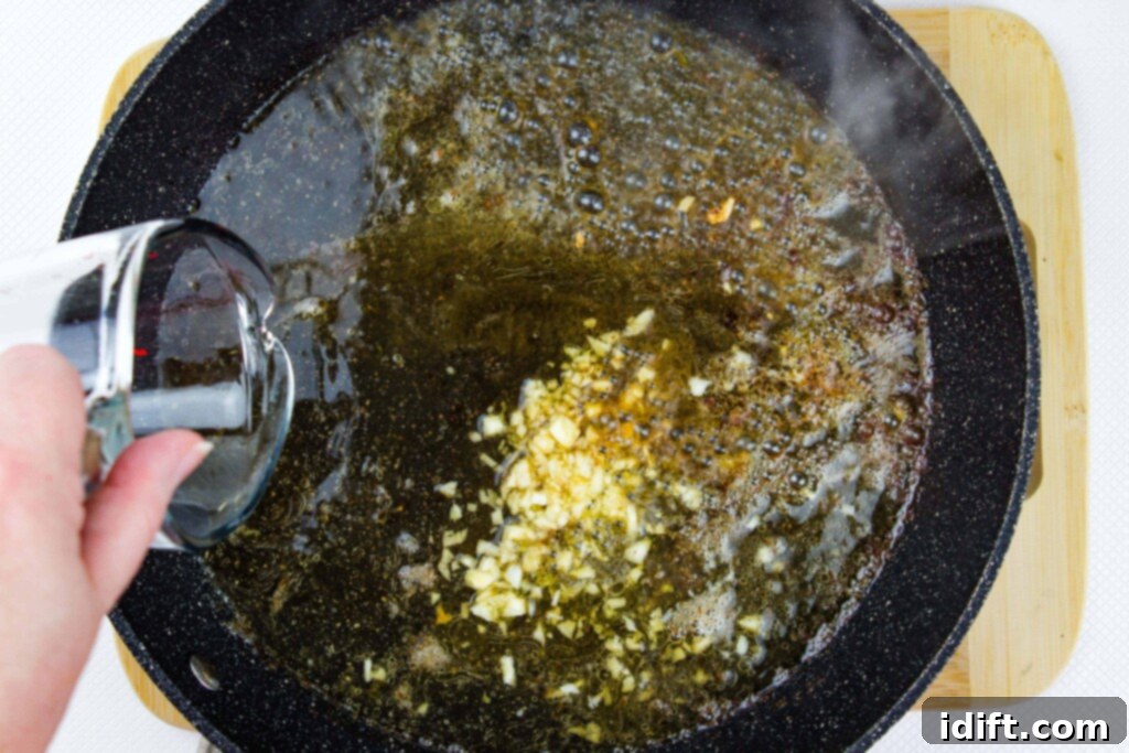 Sauteed garlic in a black skillet with white wine being poured in, beginning the deglazing process for a rich pan sauce.