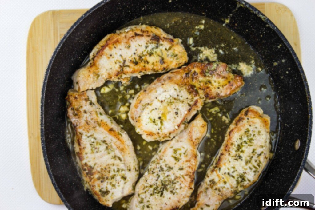Pork chops nestled in a rich wine and garlic sauce, simmering gently in a skillet to finish cooking.