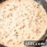 A cast iron skillet filled with creamy Queso Blanco Rotel Dip containing ground meat and diced tomatoes, ready to serve.