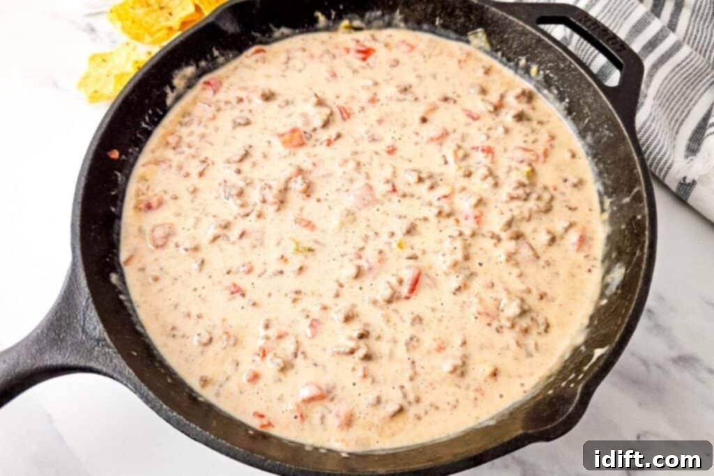 A ready-to-serve cast iron skillet filled with smooth, creamy Queso Blanco Rotel Dip, with a bowl of crispy tortilla chips visible in the background on a marble surface, inviting guests to enjoy.